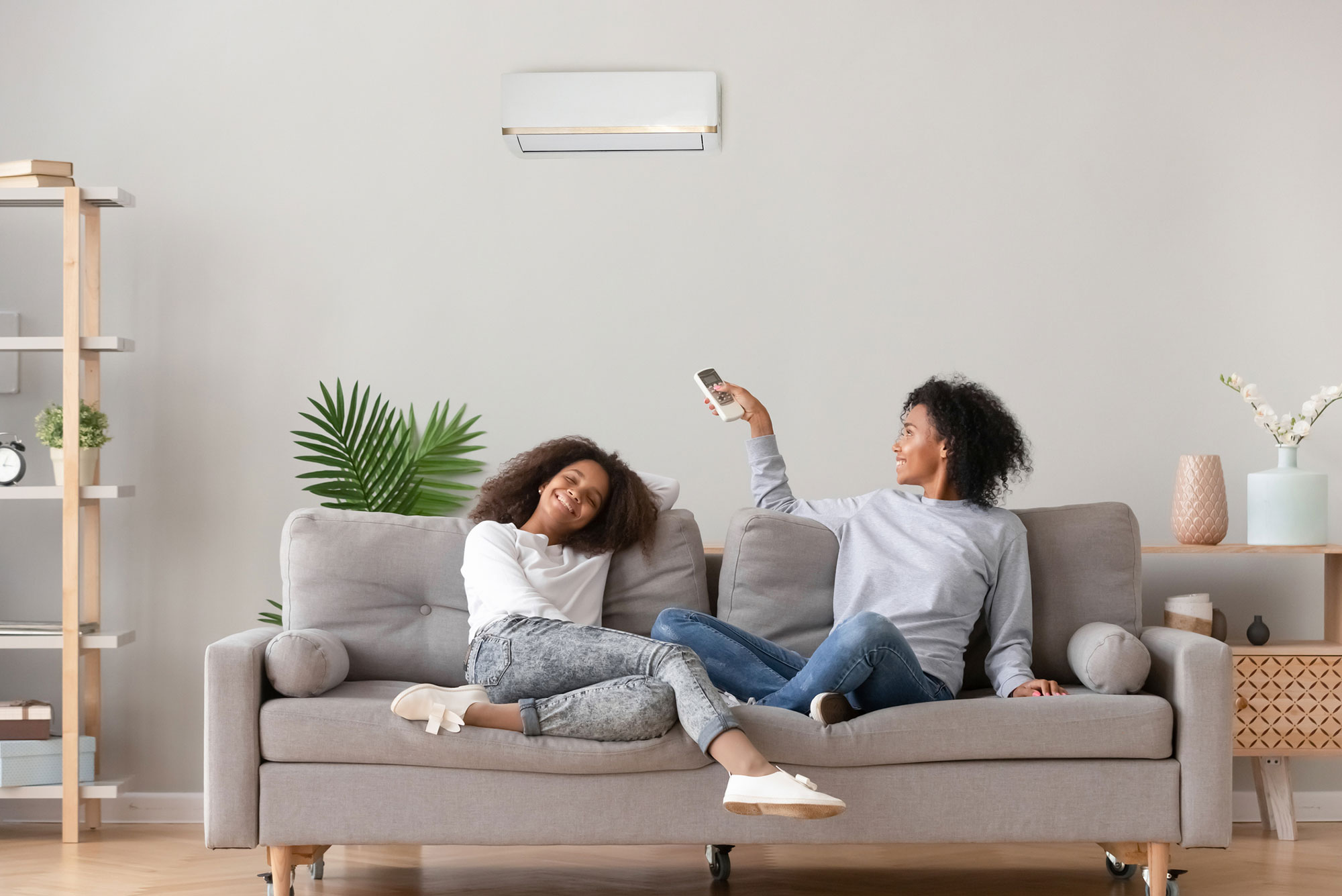 Women on couch use remote control to turn on heat pump air conditioner
